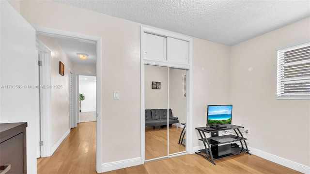 interior space featuring light wood-style floors, a textured ceiling, and baseboards