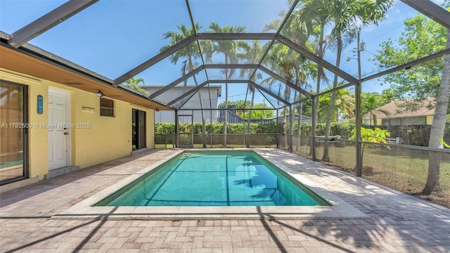 outdoor pool with a patio, glass enclosure, and fence