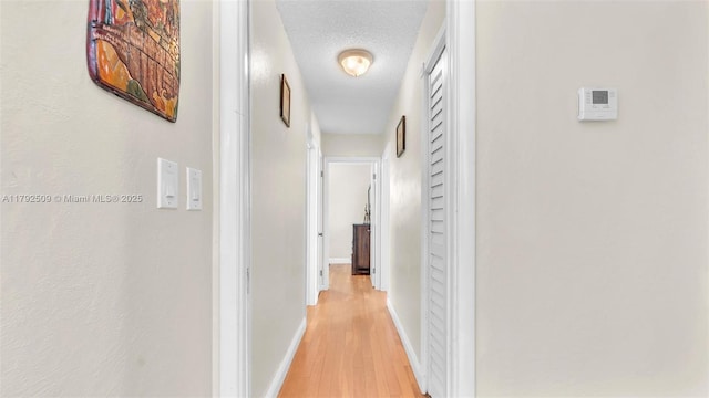 corridor with baseboards, light wood finished floors, and a textured ceiling