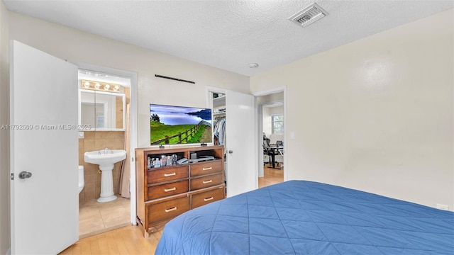 bedroom featuring a textured ceiling, visible vents, tile walls, wood finished floors, and connected bathroom