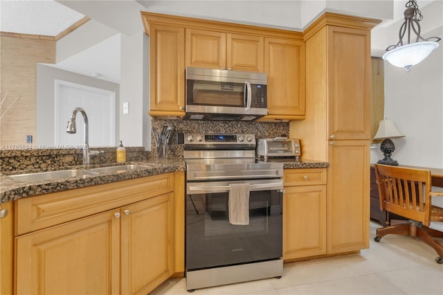 kitchen featuring a sink, dark stone counters, light tile patterned floors, and stainless steel appliances