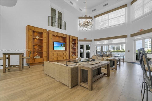living area featuring a notable chandelier, a high ceiling, visible vents, and light wood finished floors