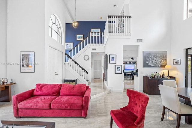 living area with stairway, visible vents, marble finish floor, and a towering ceiling