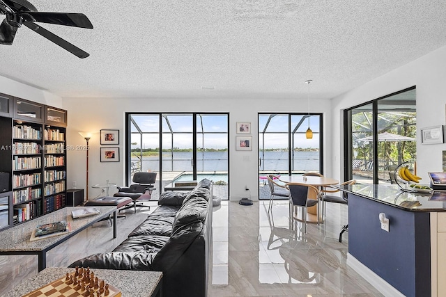 living area with a ceiling fan, a textured ceiling, a water view, and marble finish floor