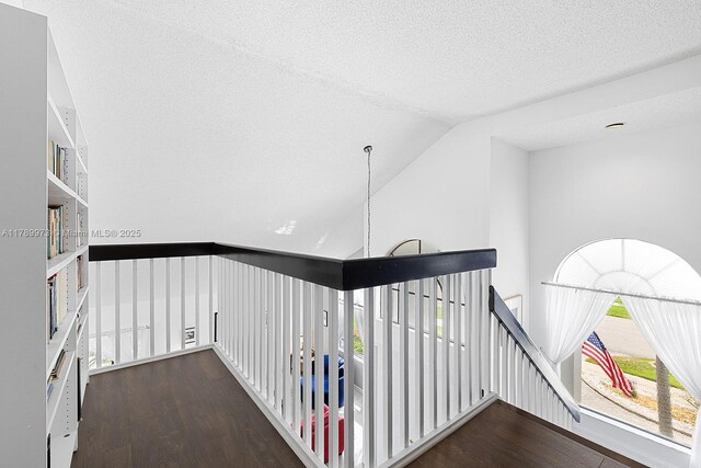hallway with a textured ceiling, an upstairs landing, wood finished floors, and lofted ceiling