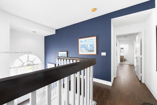 corridor with dark wood-type flooring, baseboards, and an upstairs landing