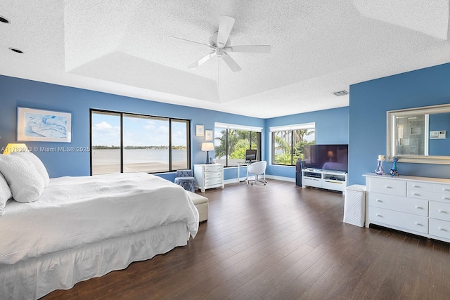 bedroom featuring a tray ceiling, dark wood finished floors, a textured ceiling, and visible vents
