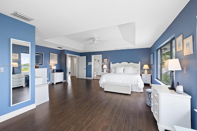 bedroom featuring visible vents, wood finished floors, baseboards, a tray ceiling, and a ceiling fan