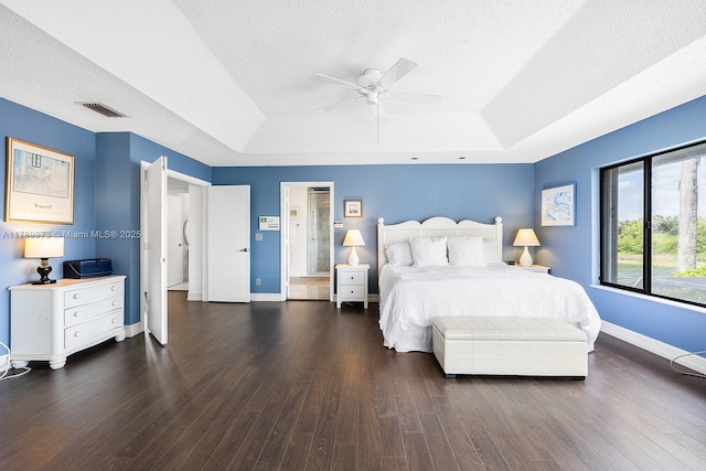 bedroom featuring a textured ceiling, baseboards, wood finished floors, a tray ceiling, and visible vents
