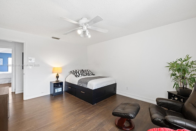 bedroom with ceiling fan, a textured ceiling, dark wood finished floors, baseboards, and visible vents