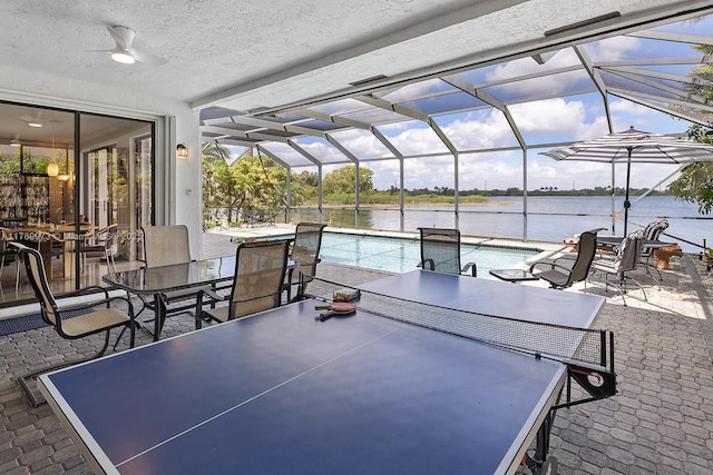 view of patio / terrace with ceiling fan, an outdoor pool, a water view, glass enclosure, and outdoor dining space