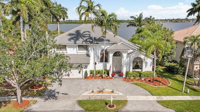 mediterranean / spanish house featuring curved driveway, a water view, stucco siding, and a tiled roof