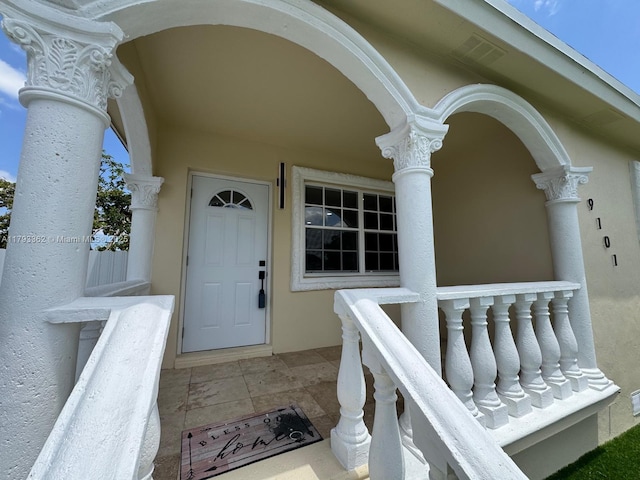 doorway to property with a porch and stucco siding