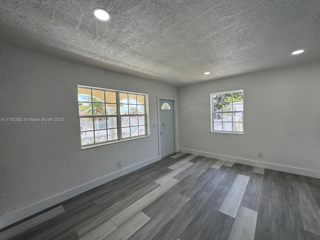 foyer entrance featuring dark wood-style flooring, a textured ceiling, baseboards, a textured wall, and recessed lighting