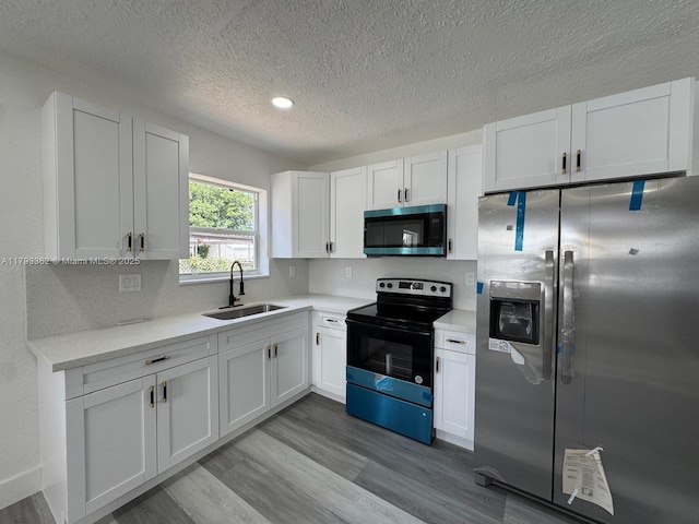 kitchen with light countertops, a textured ceiling, a sink, light wood finished floors, and appliances with stainless steel finishes