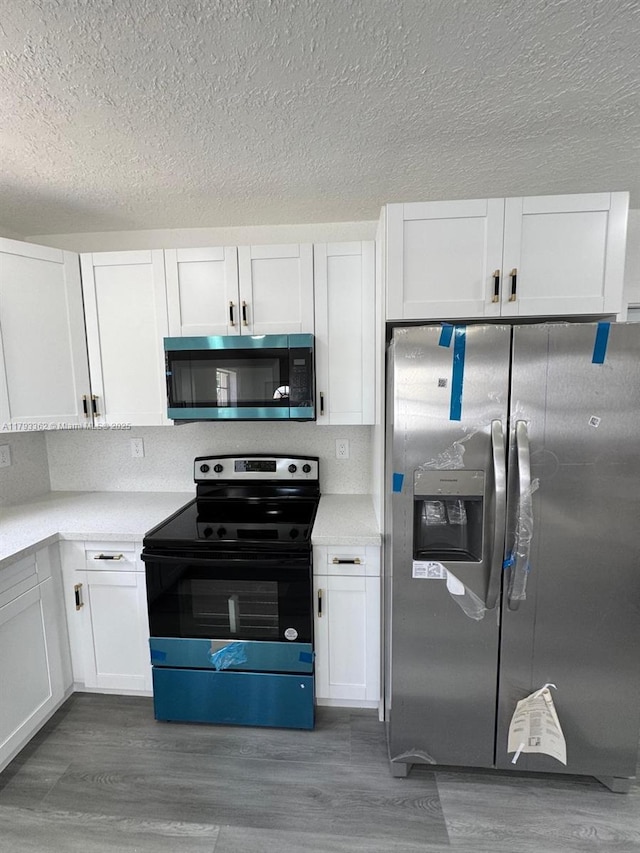 kitchen featuring a textured ceiling, wood finished floors, light countertops, stainless steel appliances, and white cabinetry