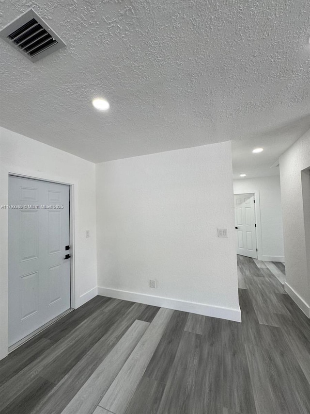 empty room with dark wood-style flooring, baseboards, visible vents, and a textured ceiling