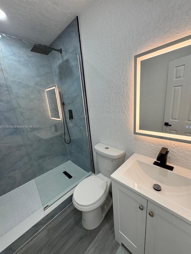 bathroom with wood finished floors, vanity, toilet, a marble finish shower, and a textured wall