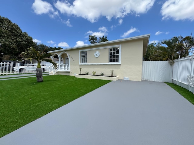 view of front of property with stucco siding, fence private yard, a patio area, and a front yard