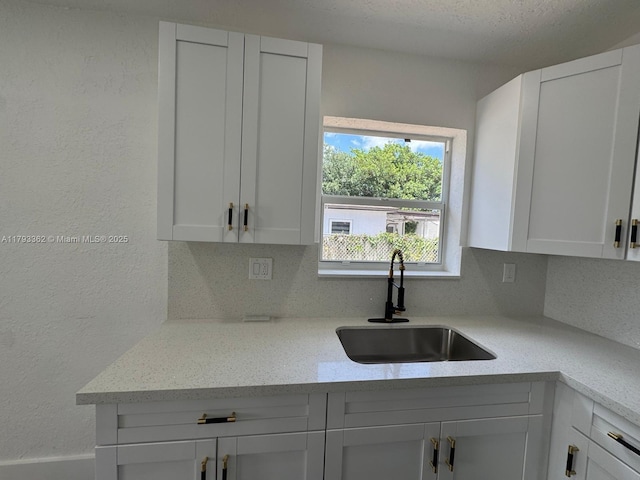 kitchen featuring a sink, a textured wall, white cabinets, and light stone countertops