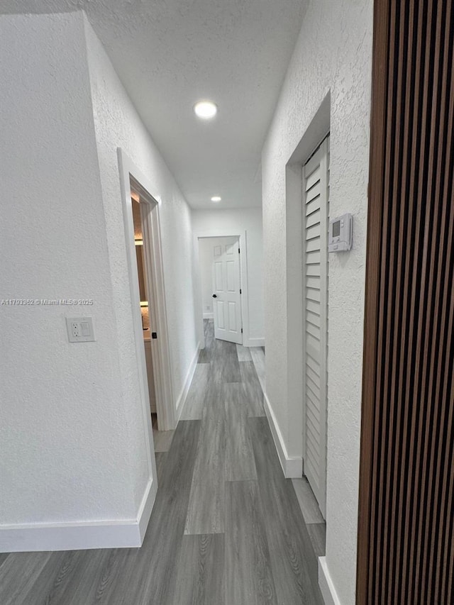 corridor featuring baseboards, a textured wall, recessed lighting, and dark wood-type flooring