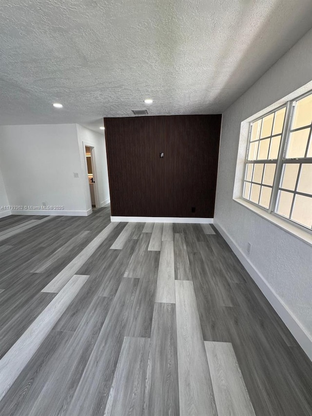 unfurnished living room featuring baseboards, a textured ceiling, and wood finished floors