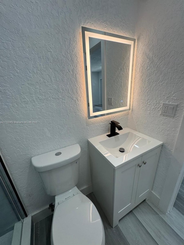 bathroom with vanity, a textured wall, wood finished floors, and toilet