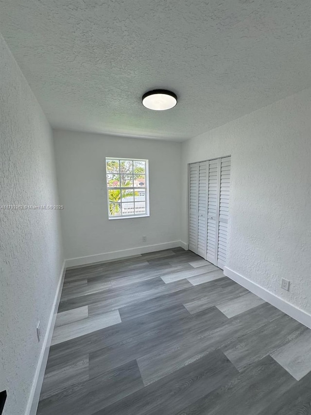 unfurnished bedroom featuring a textured ceiling, a textured wall, baseboards, and wood finished floors