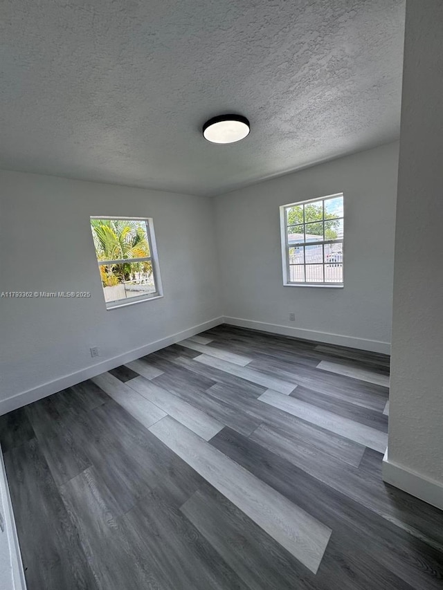 empty room with baseboards, a textured ceiling, and dark wood-type flooring