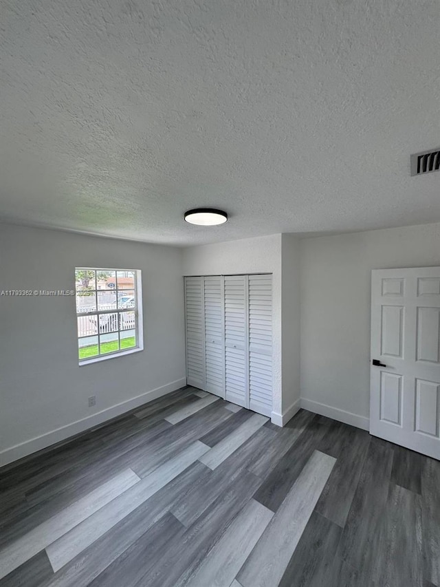 unfurnished bedroom with baseboards, dark wood-style flooring, a textured ceiling, and visible vents