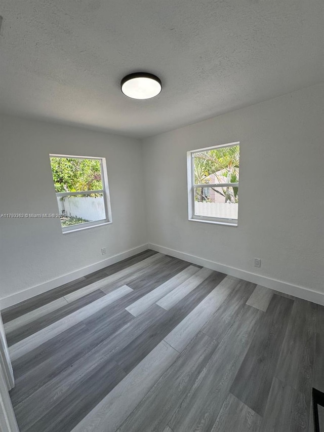 empty room with dark wood-type flooring, a textured ceiling, and a healthy amount of sunlight
