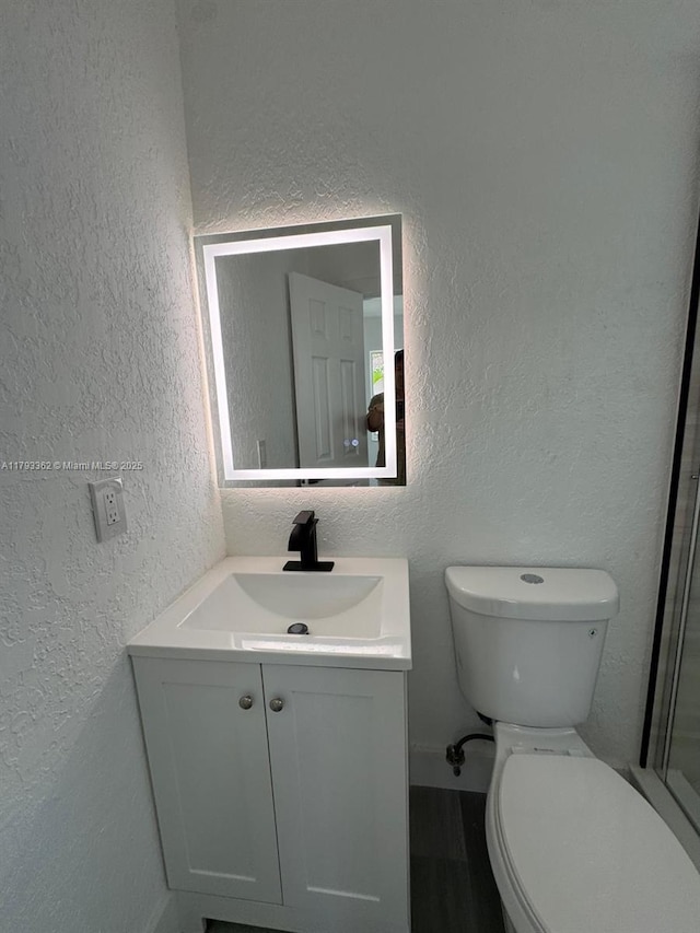 bathroom with an enclosed shower, wood finished floors, vanity, toilet, and a textured wall