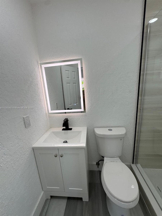 full bathroom with a stall shower, wood finished floors, vanity, toilet, and a textured wall