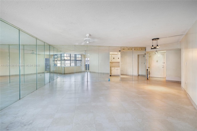 empty room featuring a textured ceiling, ceiling fan, and baseboards