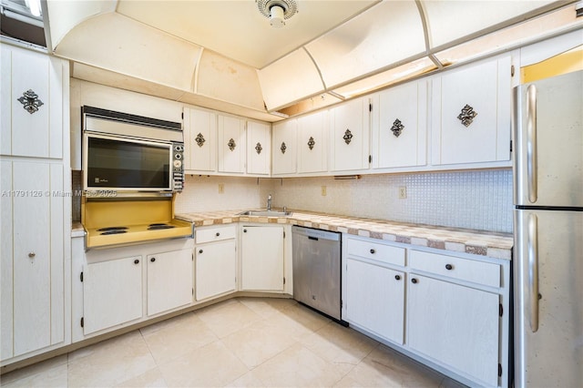 kitchen featuring appliances with stainless steel finishes, a sink, light countertops, light tile patterned floors, and backsplash