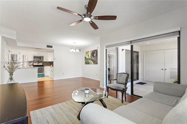 living area with visible vents, light wood-style flooring, ceiling fan with notable chandelier, and baseboards
