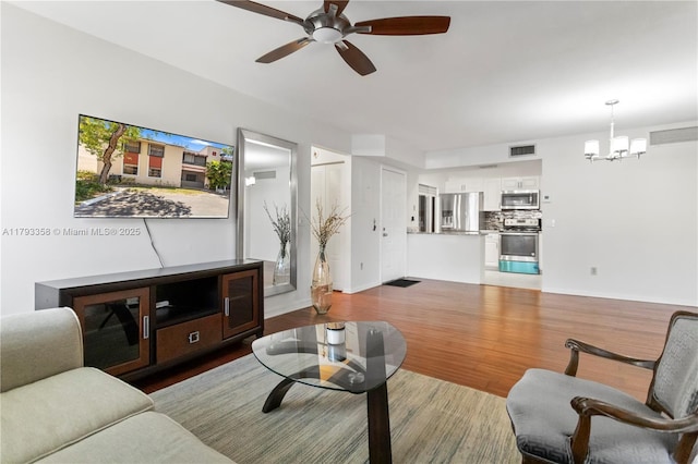 living room with baseboards, ceiling fan with notable chandelier, wood finished floors, and visible vents