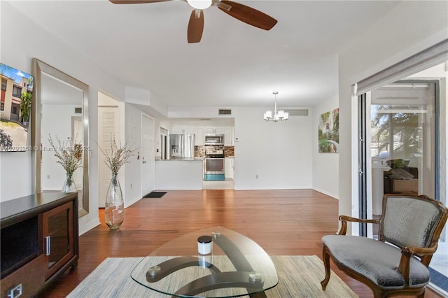 living room featuring baseboards, ceiling fan with notable chandelier, wood finished floors, and visible vents