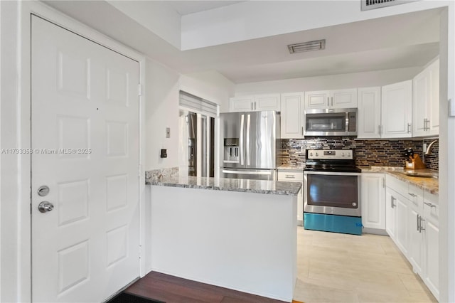 kitchen with white cabinets, appliances with stainless steel finishes, light stone counters, tasteful backsplash, and visible vents