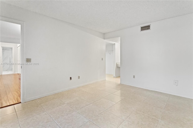empty room with a textured ceiling, baseboards, light tile patterned flooring, and visible vents