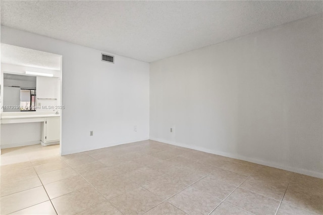 empty room with visible vents, a textured ceiling, and light tile patterned floors