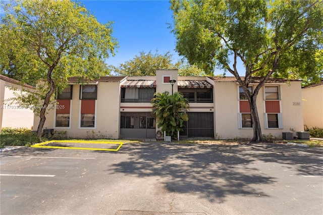view of front of property featuring central AC, uncovered parking, and stucco siding