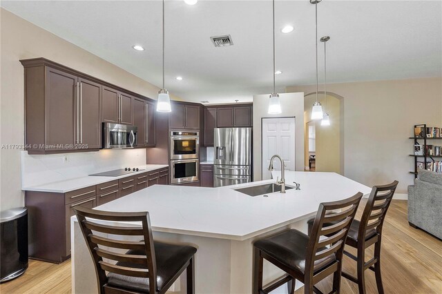 6017 NW 56th Cir, Coral Springs, FL 33067 - kitchen featuring appliances with stainless steel finishes, dark brown cabinets, light wood-style flooring, a spacious island, and light countertops