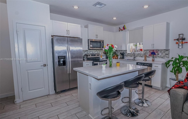 kitchen featuring appliances with stainless steel finishes, a breakfast bar, a sink, white cabinetry, and visible vents