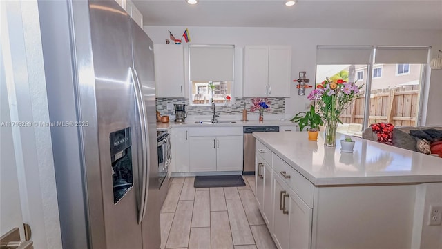 kitchen featuring a kitchen island, backsplash, appliances with stainless steel finishes, a sink, and light countertops