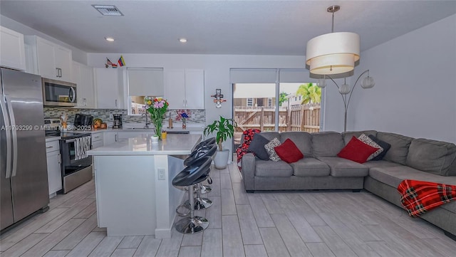 kitchen featuring open floor plan, light countertops, white cabinetry, light wood finished floors, and stainless steel appliances