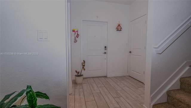 foyer featuring baseboards, stairway, and light wood-type flooring