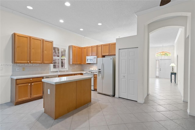 kitchen with a kitchen island, white appliances, tile counters, a sink, and backsplash