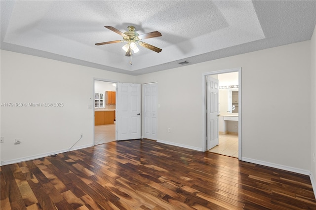 unfurnished bedroom featuring a raised ceiling, a textured ceiling, and wood finished floors