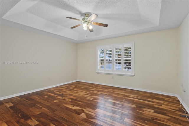 spare room with wood finished floors, baseboards, ceiling fan, a textured ceiling, and a tray ceiling